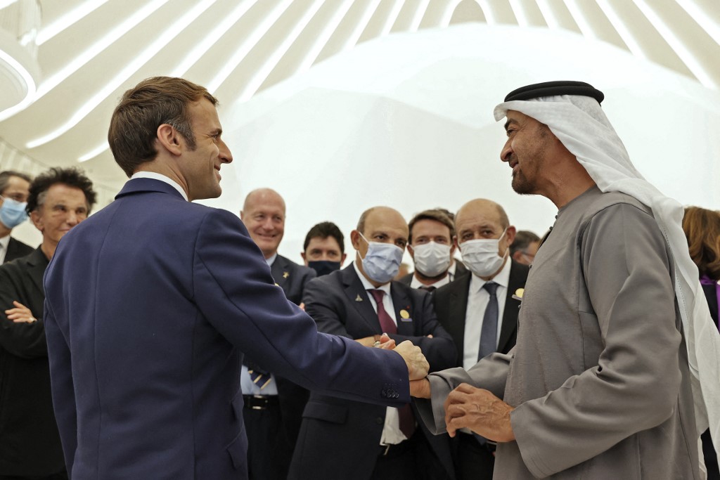 French President Emmanuel Macron (L) is greeted by Abu Dhabi's Crown Prince Mohammed bin Zayed al-Nahyan during his tour of the French pavillion at the Dubai Expo on the first day of his Gulf tour on December 3, 2021. - The UAE signed among other deals today a record, 14-billion-euro contract for 80 French-made Rafale warplanes and committed billions of euros in other agremments as Macron kicked off a Gulf tour that will also take him to Qatar and Saudi Arabia. (Photo by Thomas SAMSON / AFP)